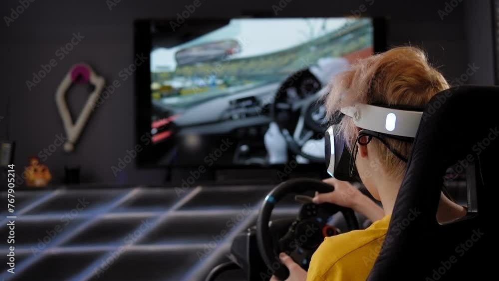 A teenager is playing a racing car game with virtual reality glasses in front of a big screen. Car driving simulator in the game room. A teenager is playing a racing car game with virtual reality glasses in front of a big screen. Car driving simulator in the game room.