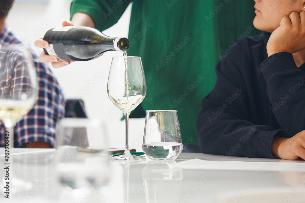 Close-up of sommelier pouring white wine into wine glass. Training and wine tasting.
