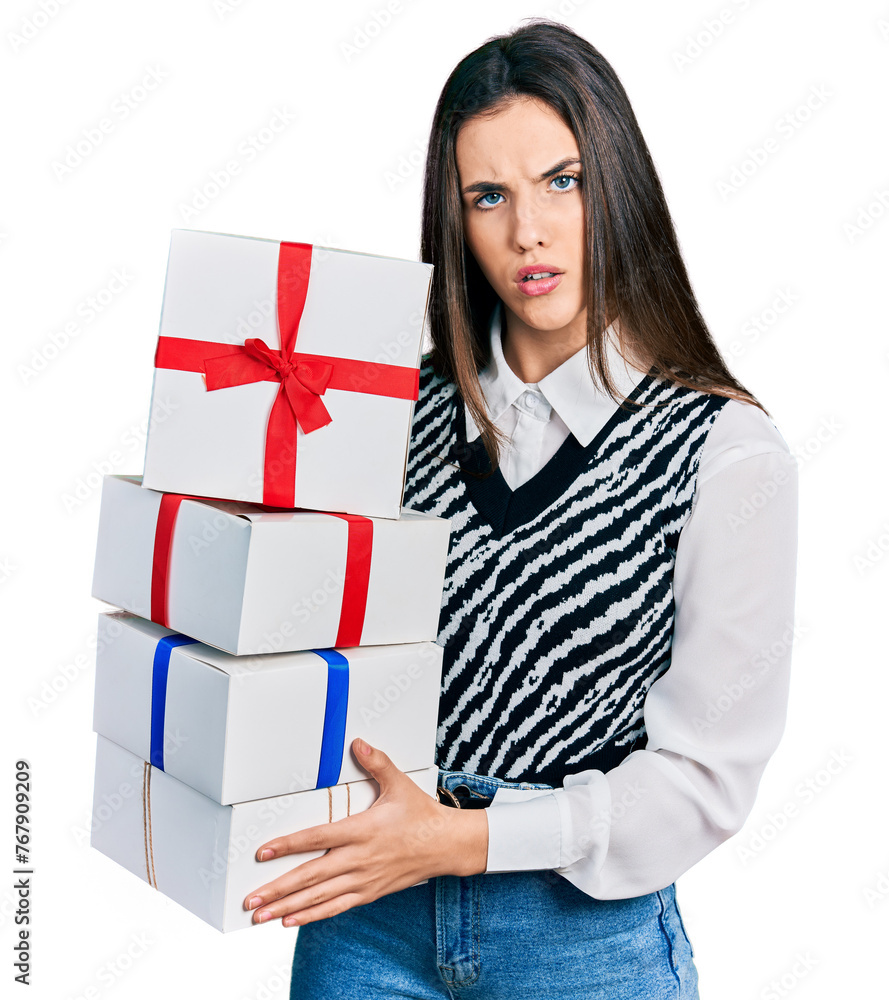 Young brunette teenager holding gifts in shock face, looking skeptical and sarcastic, surprised with open mouth Young brunette teenager holding gifts in shock face, looking skeptical and sarcastic, surprised with open mouth