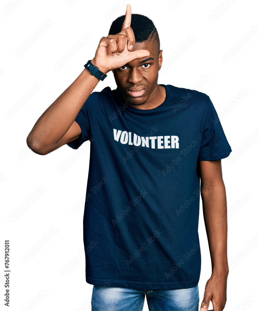 Young african american man wearing volunteer t shirt making fun of people with fingers on forehead doing loser gesture mocking and insulting. Young african american man wearing volunteer t shirt making fun of people with fingers on forehead doing loser gesture mocking and insulting.