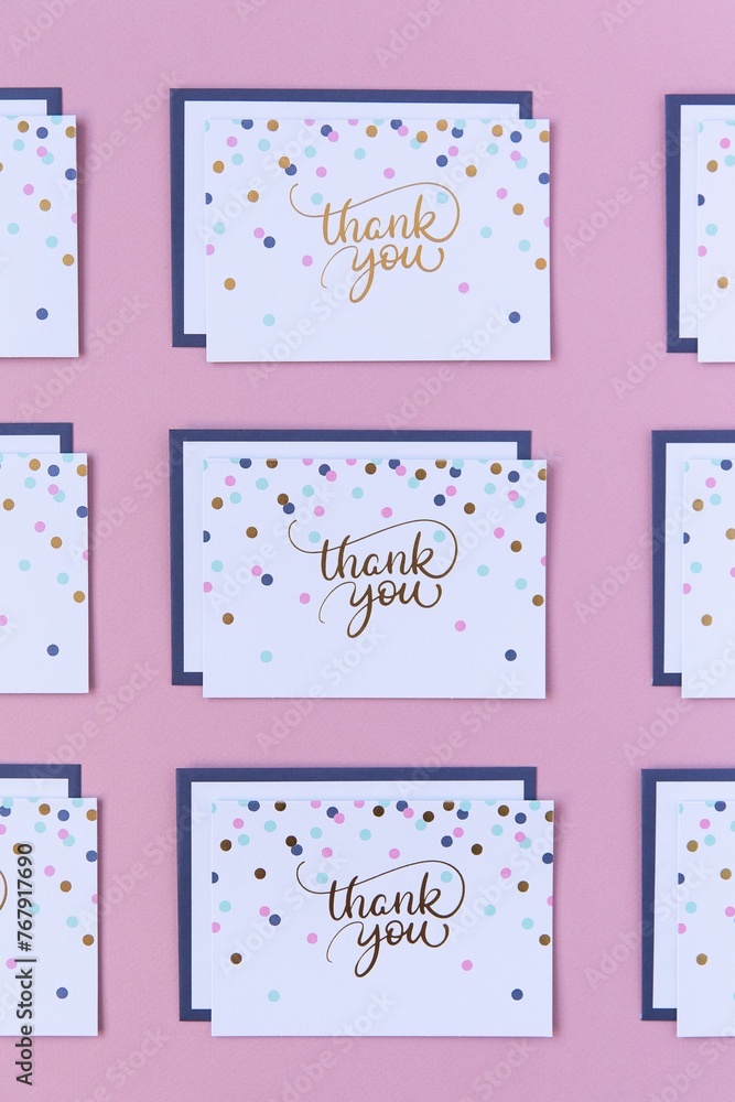 Closeup of several small thank you cards on a pink surface