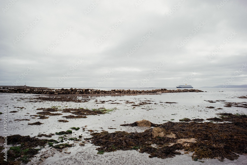 Rocky shore against a backdrop of cloudy skies with a sailboat in the background Rocky shore against a backdrop of cloudy skies with a sailboat in the background