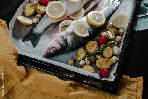 seabass fresh marinated fish with sweet onions, lemon, potatoes, cherry tomatoes and rosemarin in oven tray and baking paper ready to cook photo