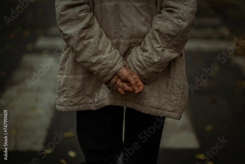 Man wearing a raincoat walking along a city street with his hands behind his back