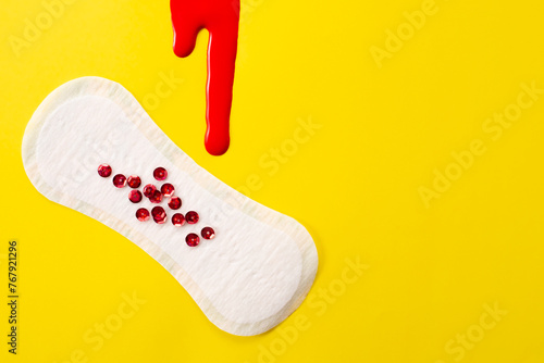 Blood and feminine hygiene pad with red glitter on yellow background. First menstrual period concept  photo