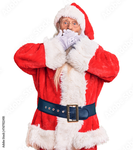 Old senior man with grey hair and long beard wearing traditional santa claus costume shocked covering mouth with hands for mistake. secret concept.