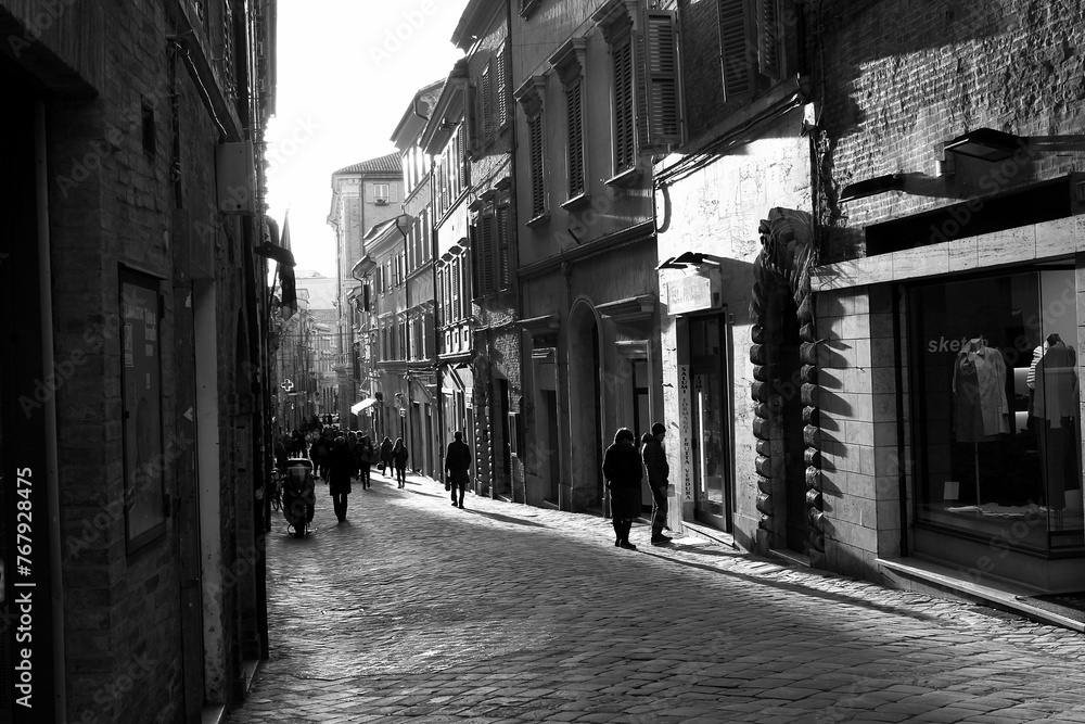 Obraz premium People walking through a quiet street in Macerata, Italy, captured in black and white