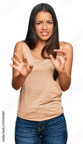 Beautiful hispanic woman wearing casual clothes disgusted expression, displeased and fearful doing disgust face because aversion reaction. with hands raised