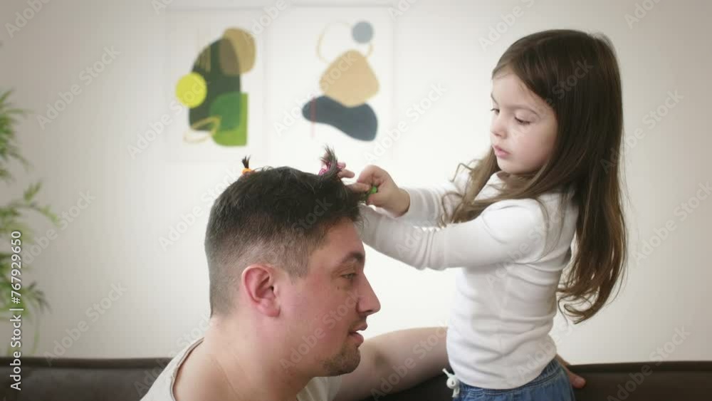 Pretty little girl makes pigtails on father head at home Pretty little girl makes pigtails on father head at home