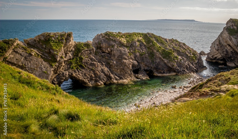 Picturesque view of a rocky cove with lush, green grass on a grassy hillside in Stair Hole, Dorset