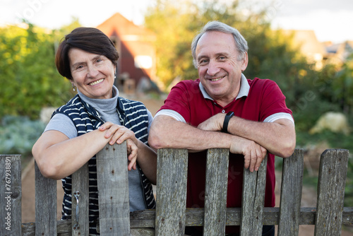 Elderly couple standing together near wooden fence in garden