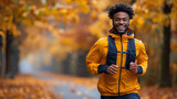 Happy man jogging in autumn park with colorful leaves, wearing a yellow jacket and backpack.