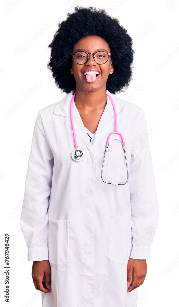 Young african american woman wearing doctor coat and stethoscope sticking tongue out happy with funny expression. emotion concept.