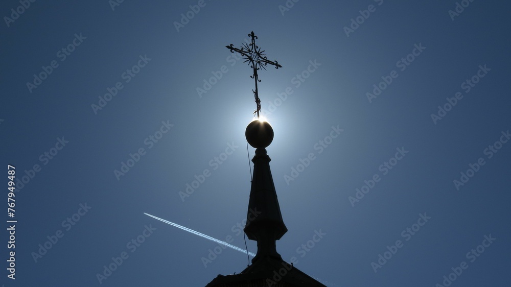 Blue sky with an airplane soaring against a tall church tower with a cross. - obrazy, fototapety, plakaty 