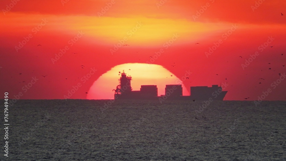 Εκτύπωση καμβά Large cargo ship in the distance silhouetted against the background of the setting sun