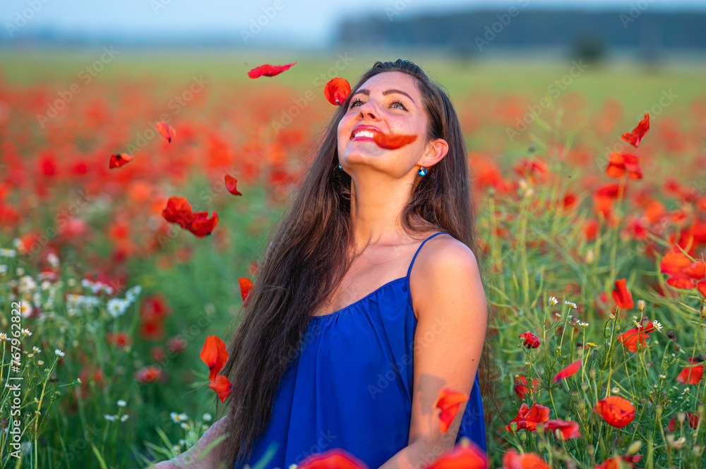 pretty young woman with long hair playing with petals in poppy field in evening sunlight pretty young woman with long hair playing with petals in poppy field in evening sunlight