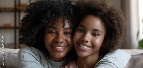Happy young African American mom hug teenage daughter making picture together, smiling black mother and teen girl sit on couch posing for photo, parent and child embrace as best friends © AI_images