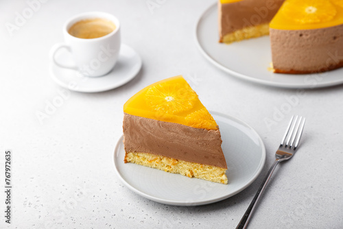 Chocolate-orange mousse cake with biscuit base, jelly and orange circles. Piece of homemade cheesecake and a cup of coffee. Traditional holiday dessert. Selective focus, close-up.