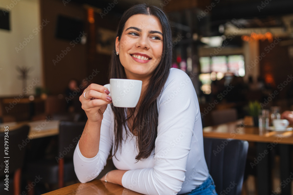 A one young girl or woman is drinking coffee in cafe or restaurant while using her phone to send messages A one young girl or woman is drinking coffee in cafe or restaurant while using her phone to send messages