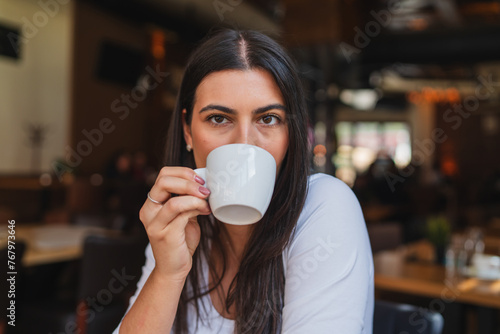 A one young girl or woman is drinking coffee in cafe or restaurant while using her phone to send messages