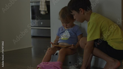 Toddler girl uses the potty watching shows on smart phone as older brother watches photo
