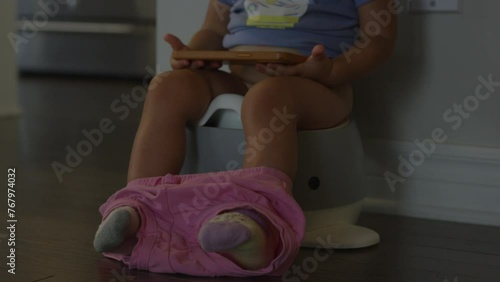 Toddler girl watching smart phone while learning to potty - hand held shot