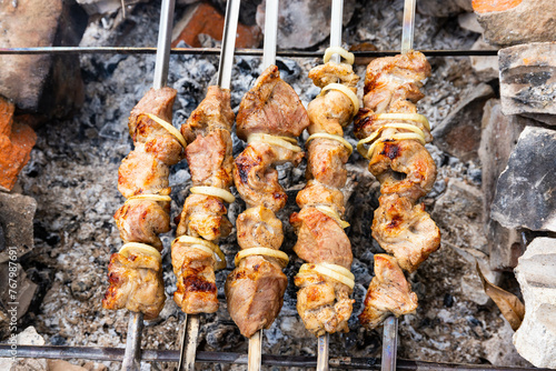 Pig shashlik with onions on a skewer. Picnic. Fried meat on fire. Background image, copy space.