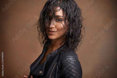 Fashion, portrait and leather jacket with woman, aesthetic and stylish clothes on brown studio background. Face, Indian person and model with mockup space and happy girl with bold and cool makeup