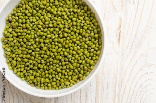 Green mung beans in a ceramic bowl on a white wooden background. Organic legumes. The concept of healthy eating. Horizontal orientation. Copy space. Top view. Selective focus.