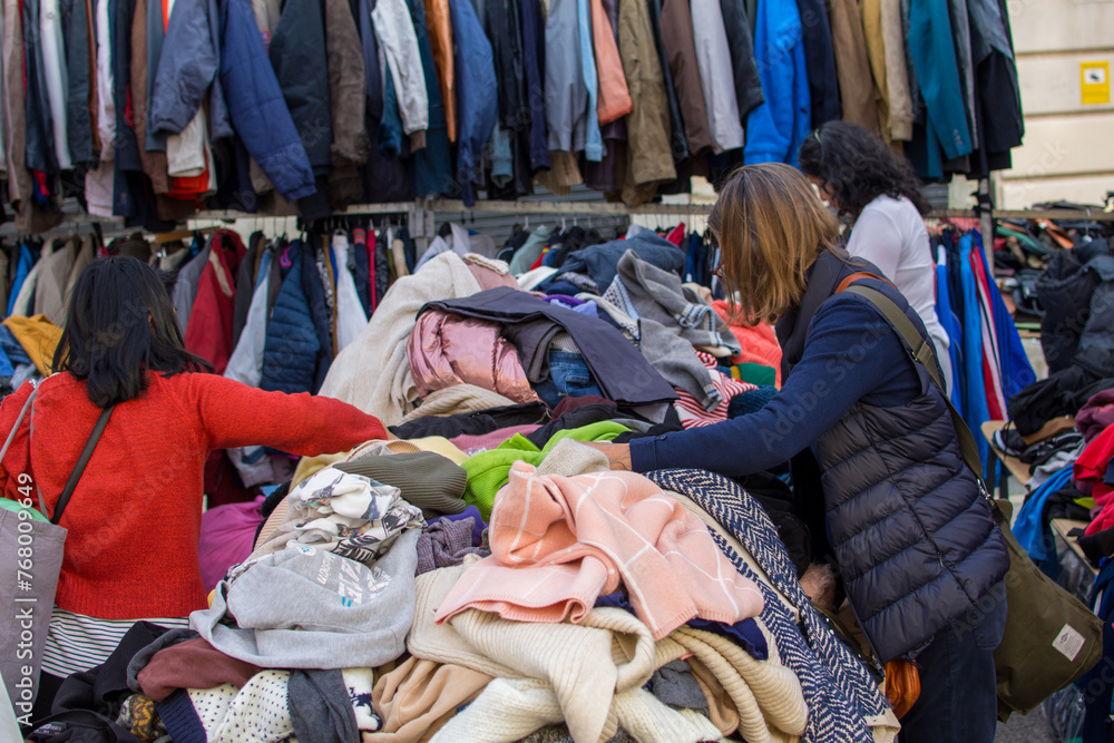 Back view of people looking at a pile of second hand clothes in a flea market. Back view of people looking at a pile of second hand clothes in a flea market.