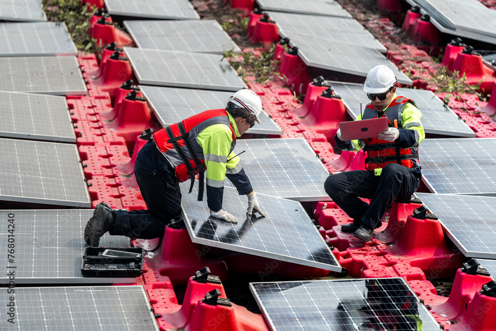 Obraz premium Male workers repair Floating solar panels on water lake. Engineers construct on site Floating solar panels at sun light. clean energy for future living. Industrial Renewable energy of green power.