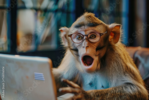 A monkey wearing glasses is looking at a laptop. A monkey with glasses working in an office. Human characters through animals. Creative idea. Shocked, startled look with wide open mouth, bulging eyes