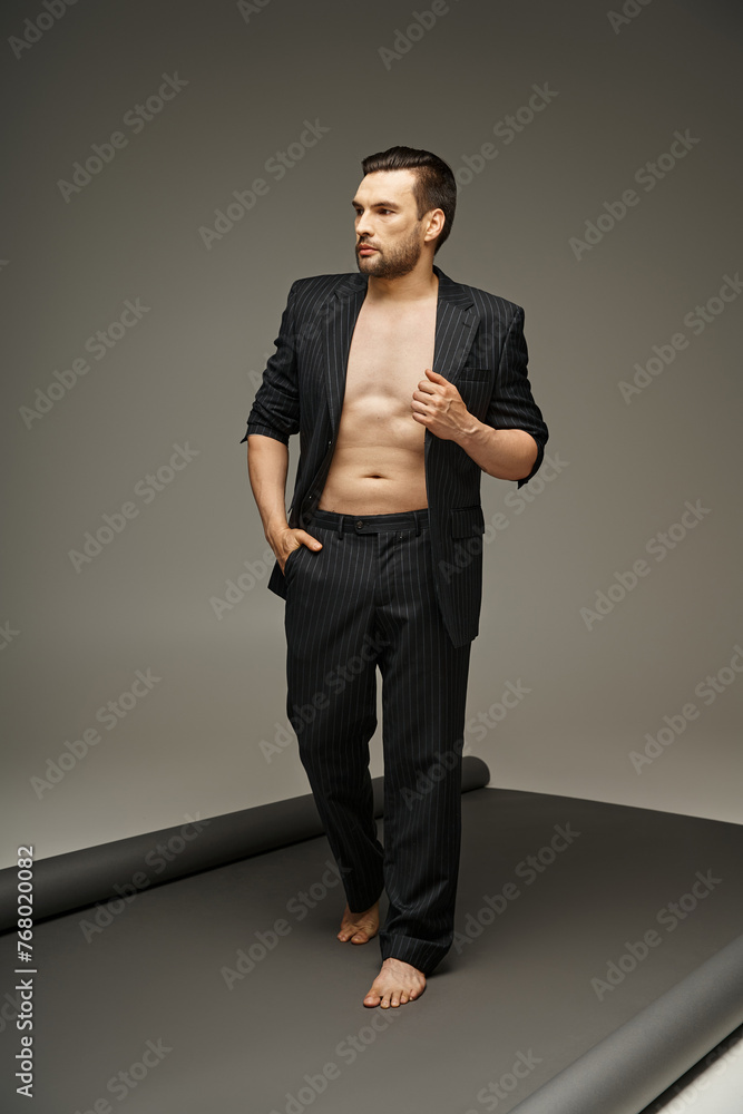 fashion statement, barefoot and shirtless man in pinstripe suit posing on grey background fashion statement, barefoot and shirtless man in pinstripe suit posing on grey background