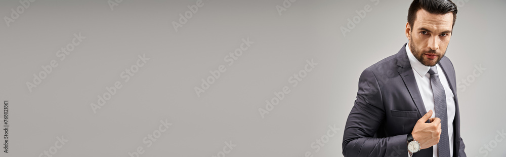 Charismatic businessman in suit with a confident stance looking at camera on grey background, banner Charismatic businessman in suit with a confident stance looking at camera on grey background, banner