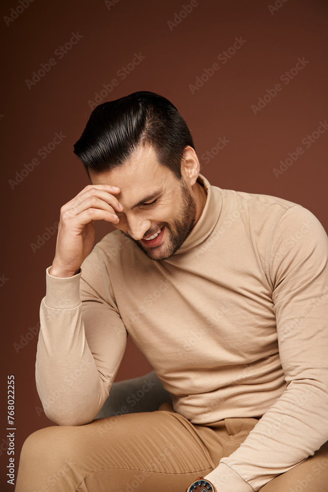 shy and handsome man in turtleneck sitting on comfortable armchair and smiling on beige background shy and handsome man in turtleneck sitting on comfortable armchair and smiling on beige background