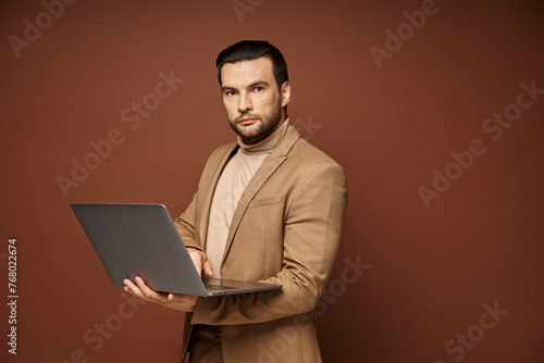 focused and handsome businessman holding his laptop while working remotely on beige background