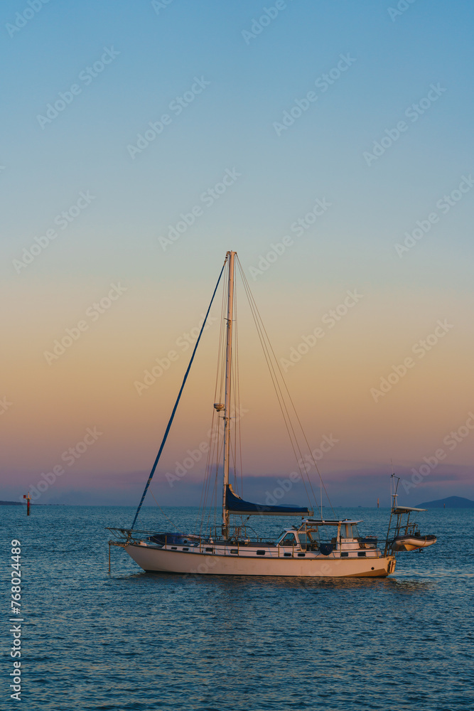 A sailboat is floating on the ocean with a beautiful sunset in the background