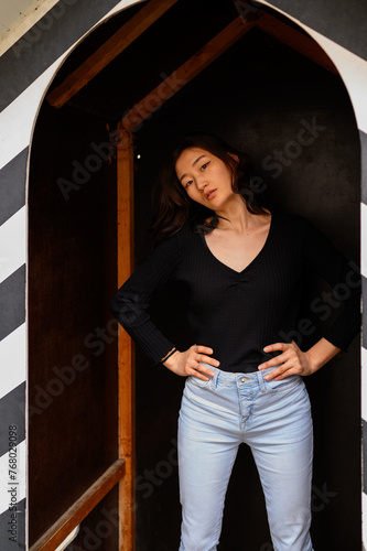 A young woman in a chic black top and light blue jeans poses in a unique architectural doorway with a black and white checkered pattern.