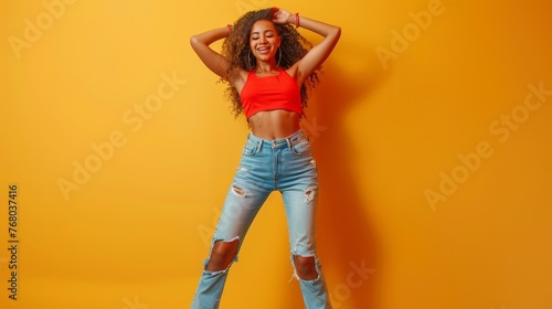 Energized happy girl raises hands joyfully, being in high spirit, dances music, has slim figure, dressed in casual clothes, poses against yellow background, jumps playfully photo