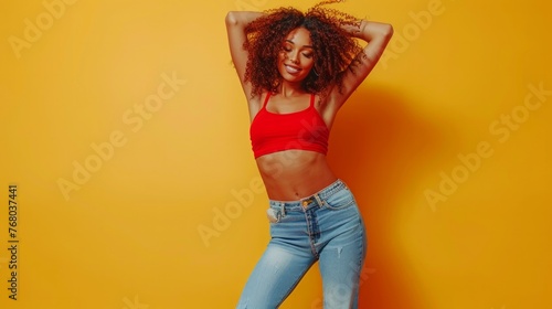 Energized happy girl raises hands joyfully, being in high spirit, dances music, has slim figure, dressed in casual clothes, poses against yellow background, jumps playfully photo