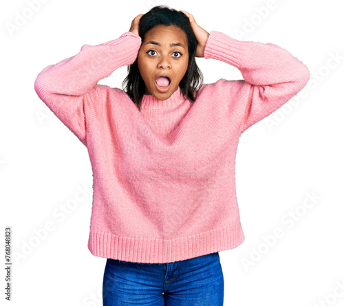 Beautiful hispanic woman wearing casual winter sweater crazy and scared with hands on head, afraid and surprised of shock with open mouth