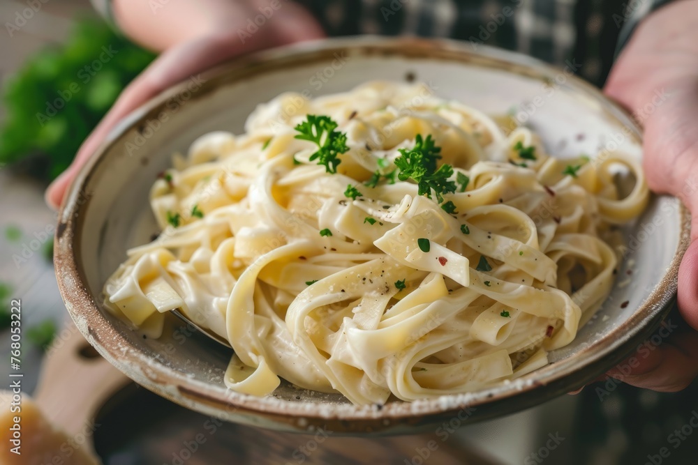 Close-up shot of hands holding a bowl of pasta topped with parsley
