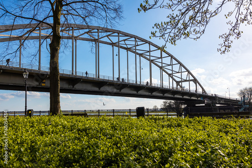 Arch bridge in Deventer seen from below with cyclists and walkers with greenery in the foreground and clear blue sky