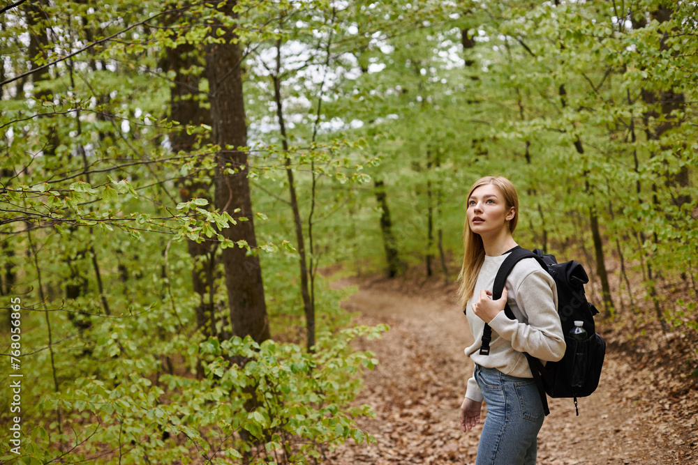 Portrait of young blonde female traveler hiking in beautiful forest and standing on a path Portrait of young blonde female traveler hiking in beautiful forest and standing on a path
