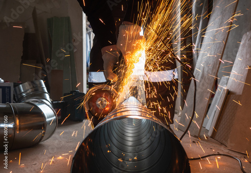 a worker cuts a ventilation pipe with an angle grinder