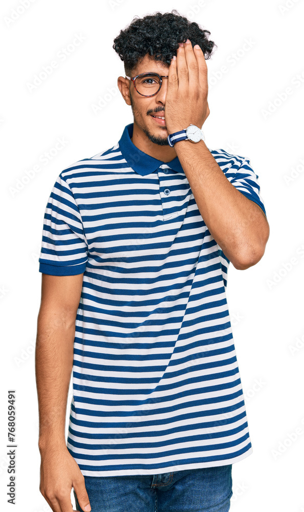 Young arab man wearing casual clothes and glasses covering one eye with hand, confident smile on face and surprise emotion. Young arab man wearing casual clothes and glasses covering one eye with hand, confident smile on face and surprise emotion.