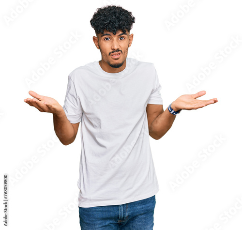 Young arab man wearing casual white t shirt clueless and confused with open arms, no idea concept. photo