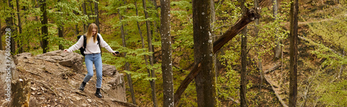 Young blonde woman wearing backpack on hiking and walking on rocky cliff with down  banner