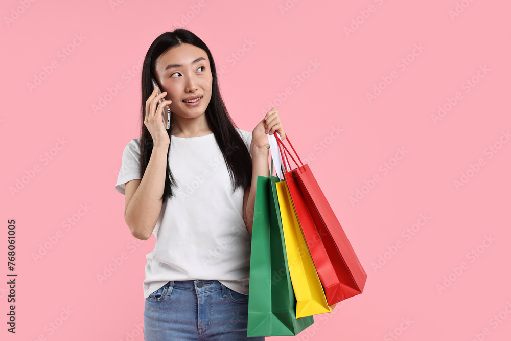 Smiling woman with shopping bags talking by smartphone on pink background. Space for text Smiling woman with shopping bags talking by smartphone on pink background. Space for text