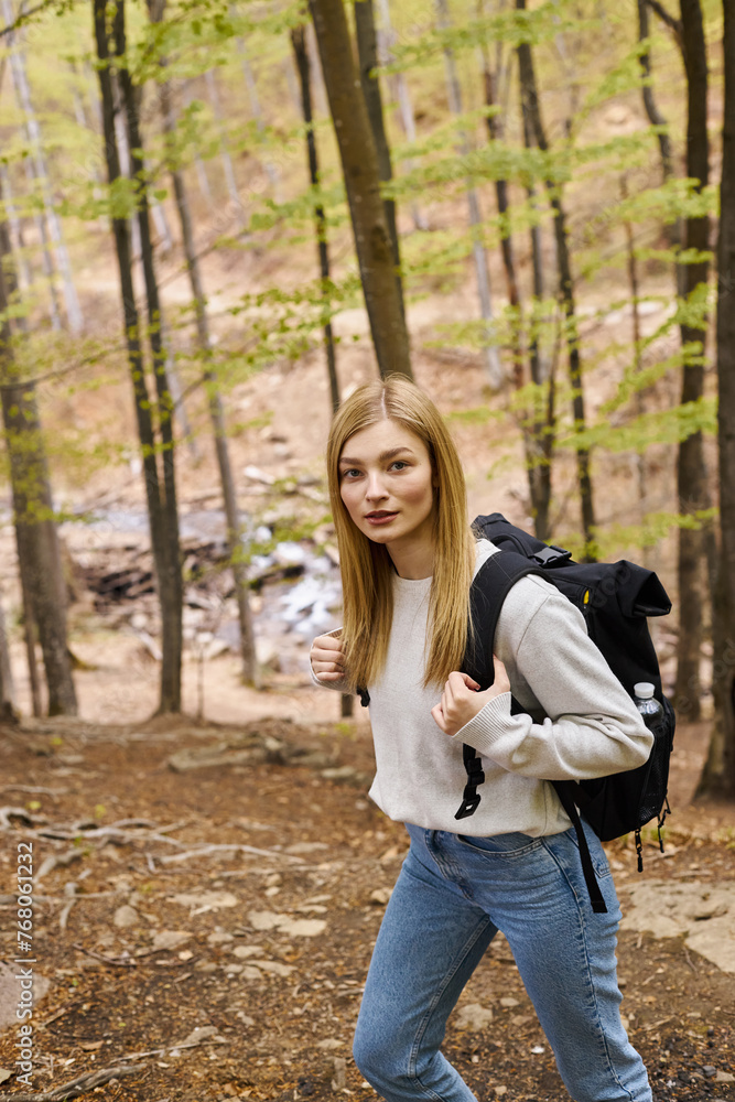 Curious blonde trekker with travel backpack, weaving through the woods looking at camera Curious blonde trekker with travel backpack, weaving through the woods looking at camera